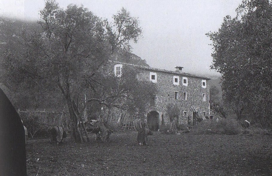 Old photograph: women gathering olives in front of the stone house, among the olive trees